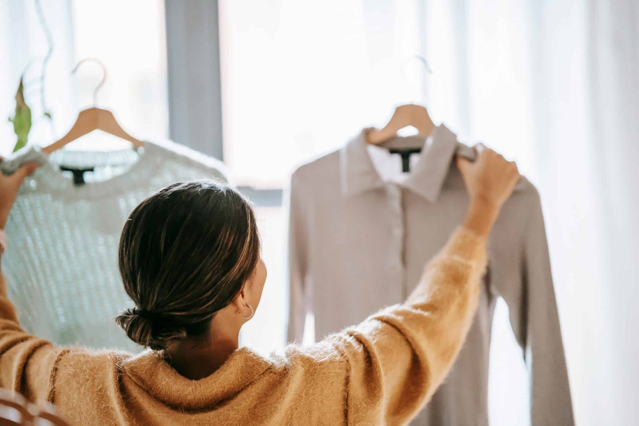 A woman shopping, holding up two sweaters from a store.