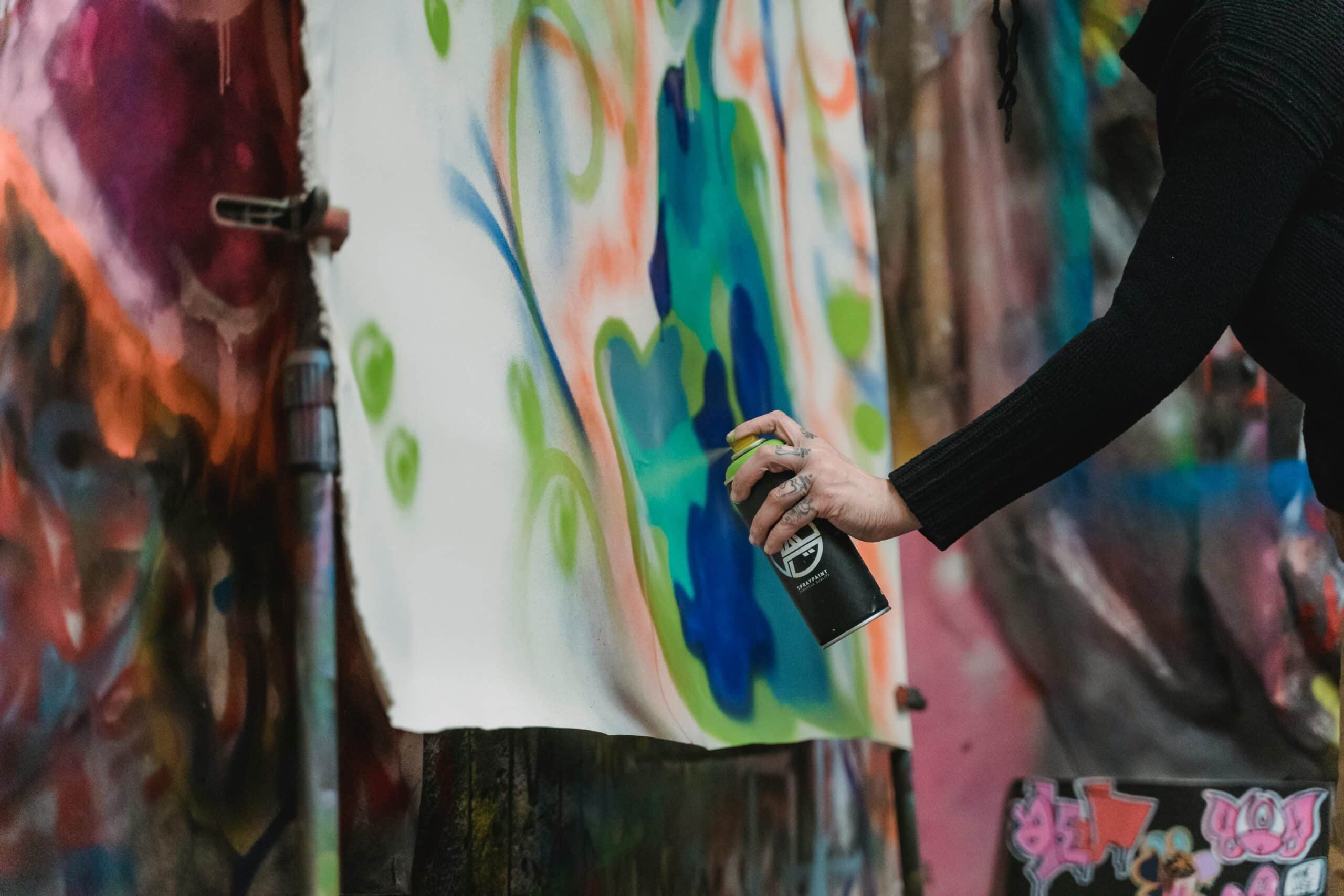 An artist spray-painting a colorful mural on a canvas in an urban setting.