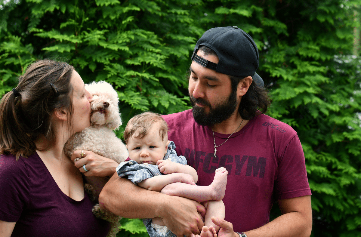 A young family holding a dog and a baby