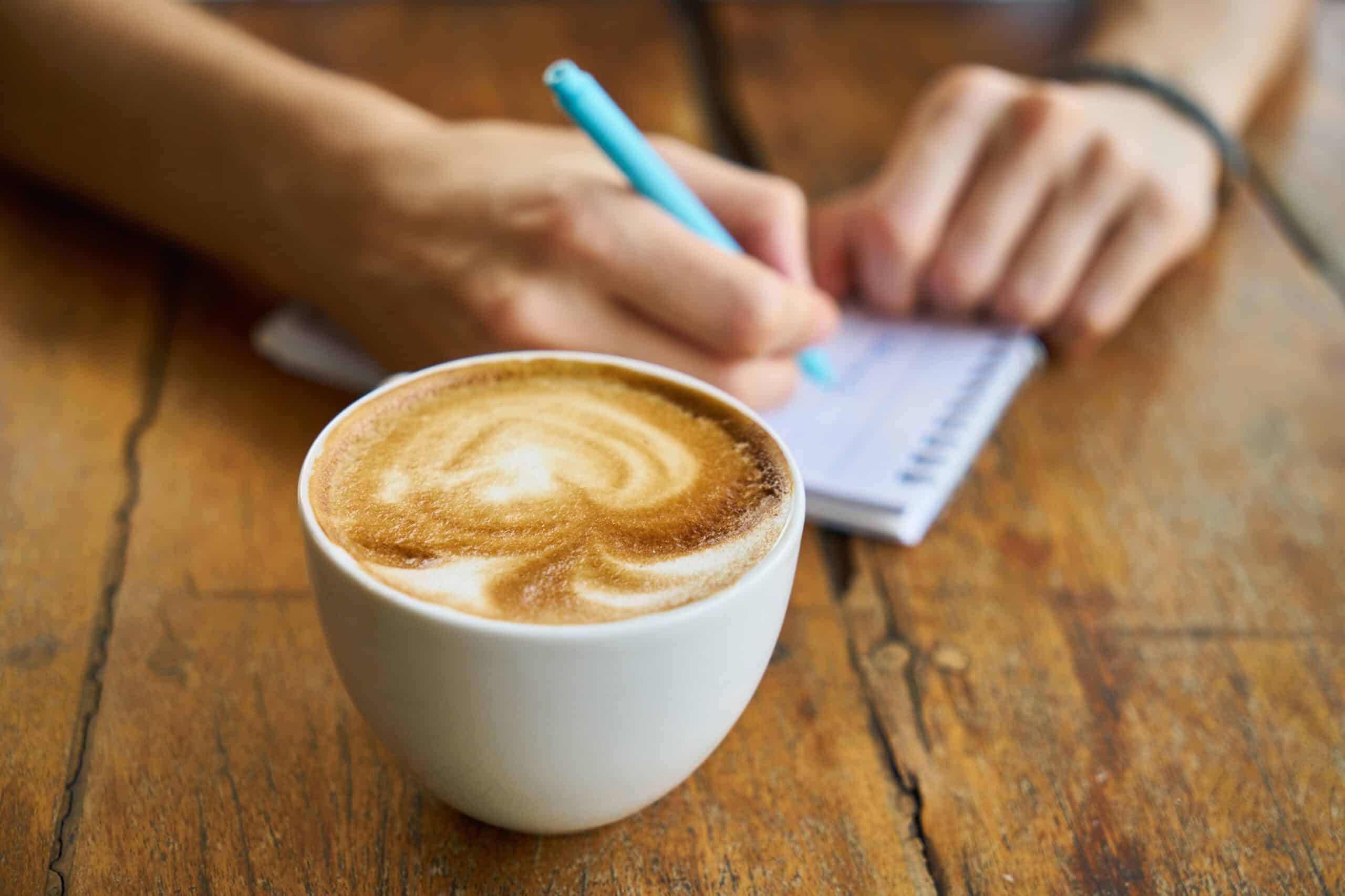 A person taking notes with a latte in front.