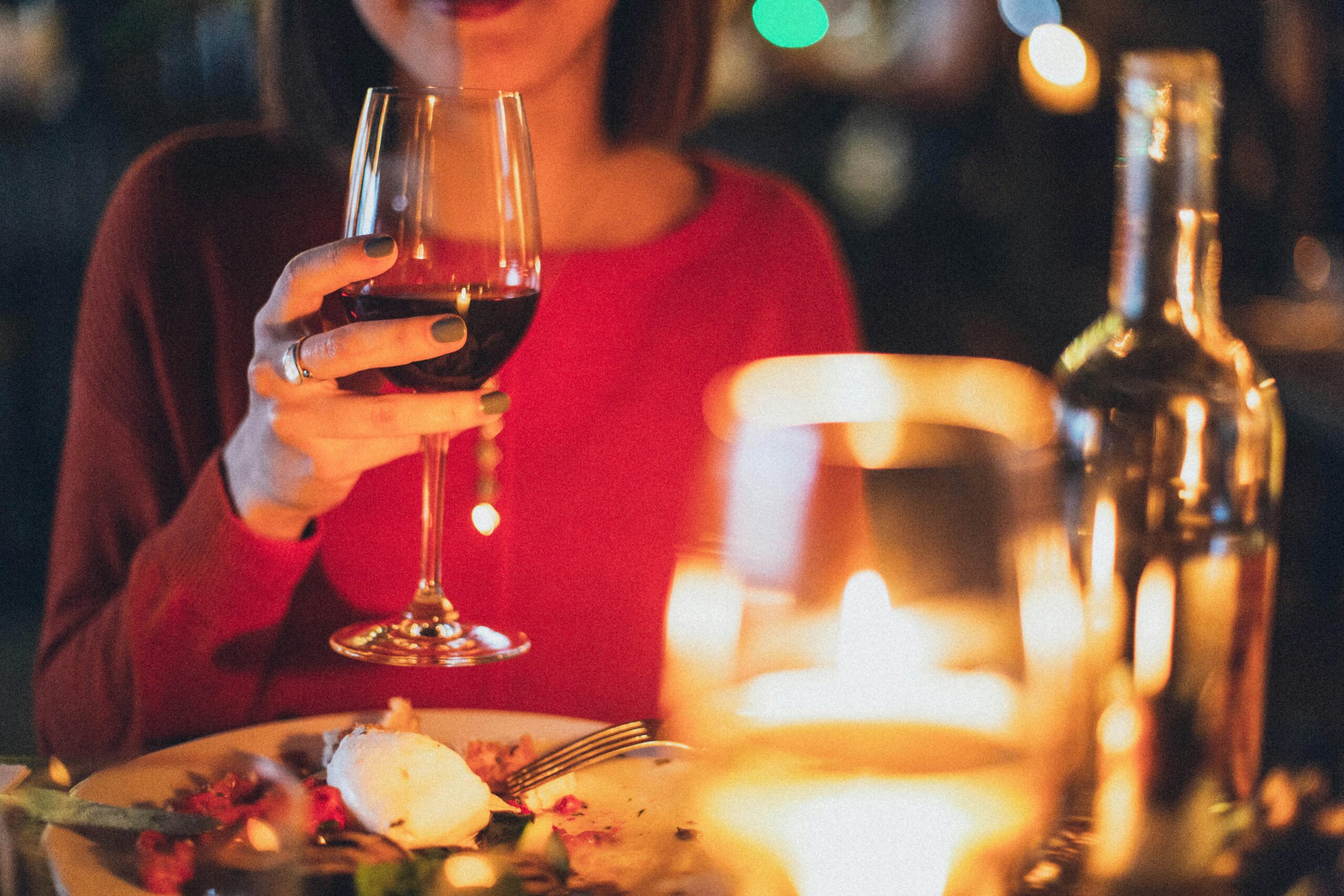 Woman in a red shirt holding a glass of red wine at dinner