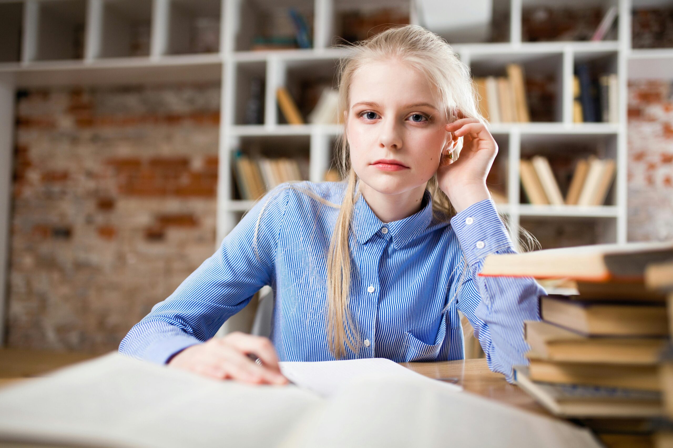 Blonde student sitting at desk with a notebook and a pencil.