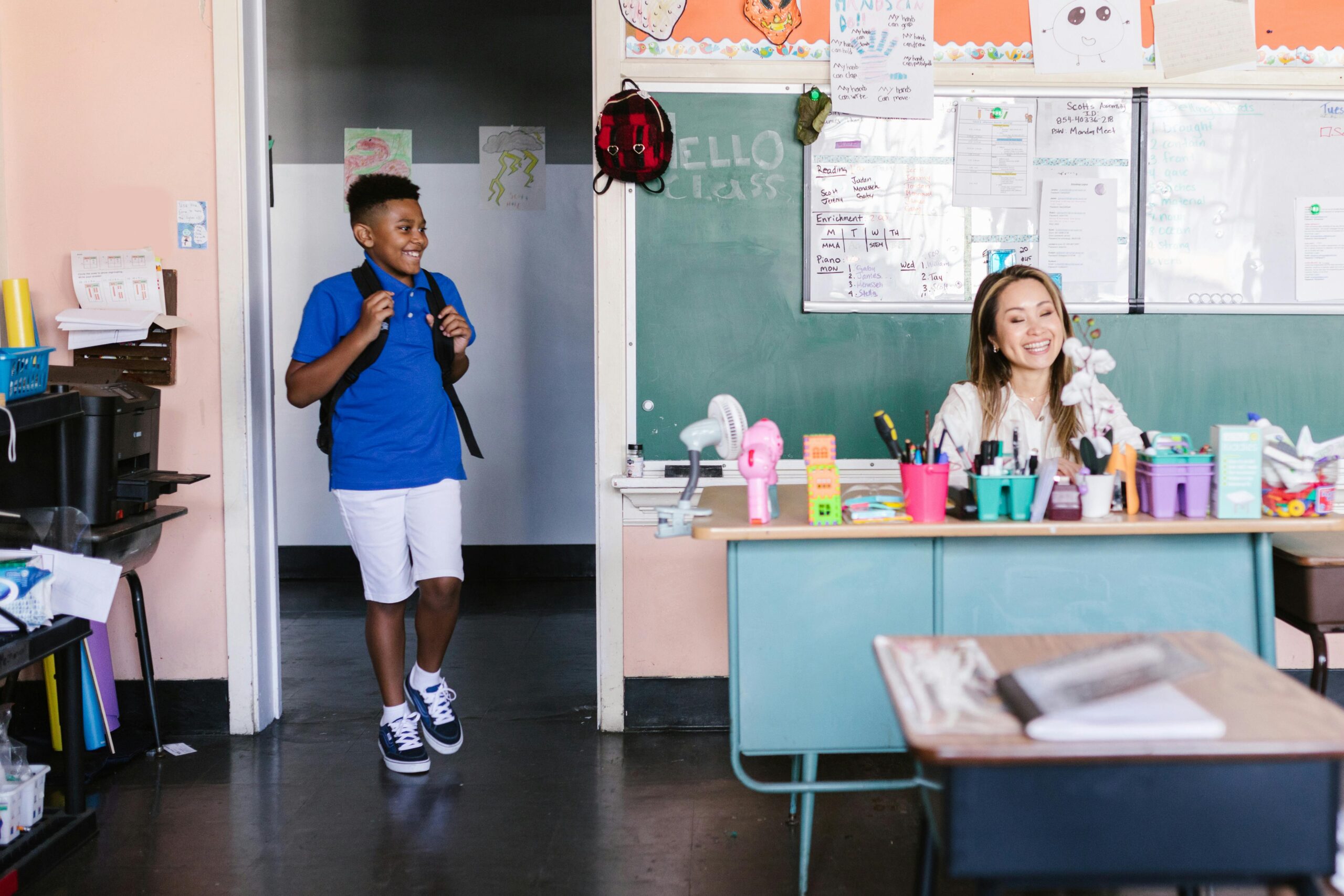 Kid walking into classroom with teacher at her desk.