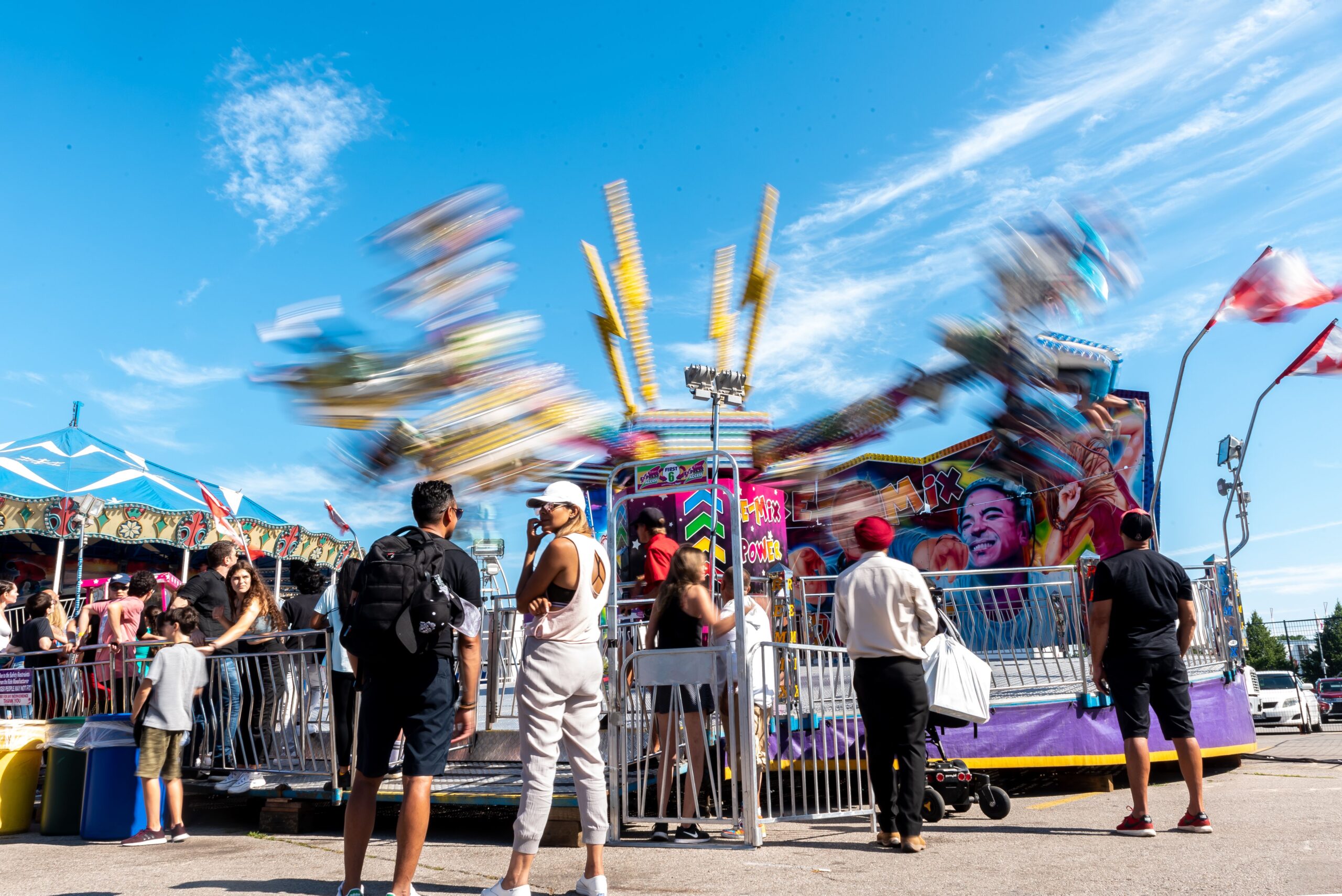 Two people talking to eachother at a festival with a blurred ride in the background.