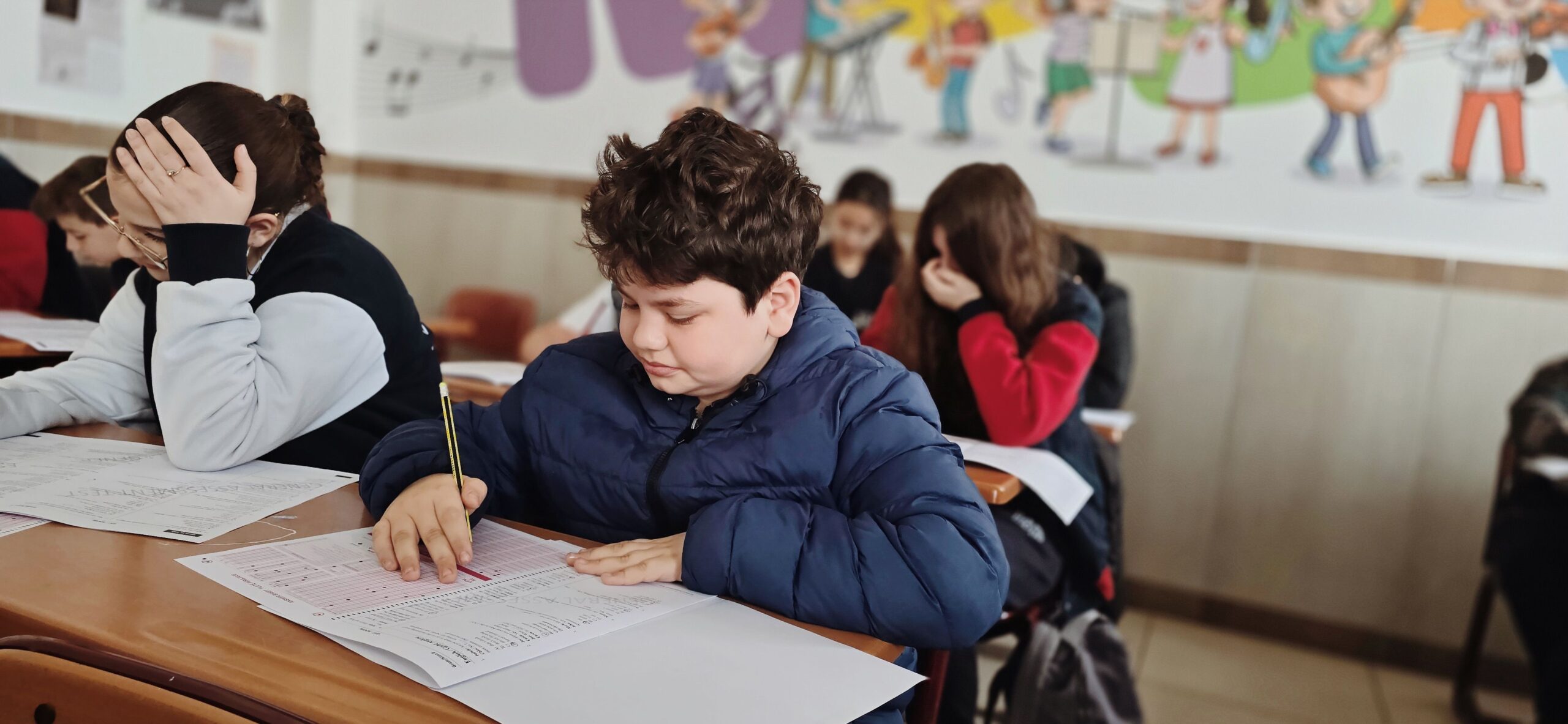 Student sitting at his desk writing with other students in the background