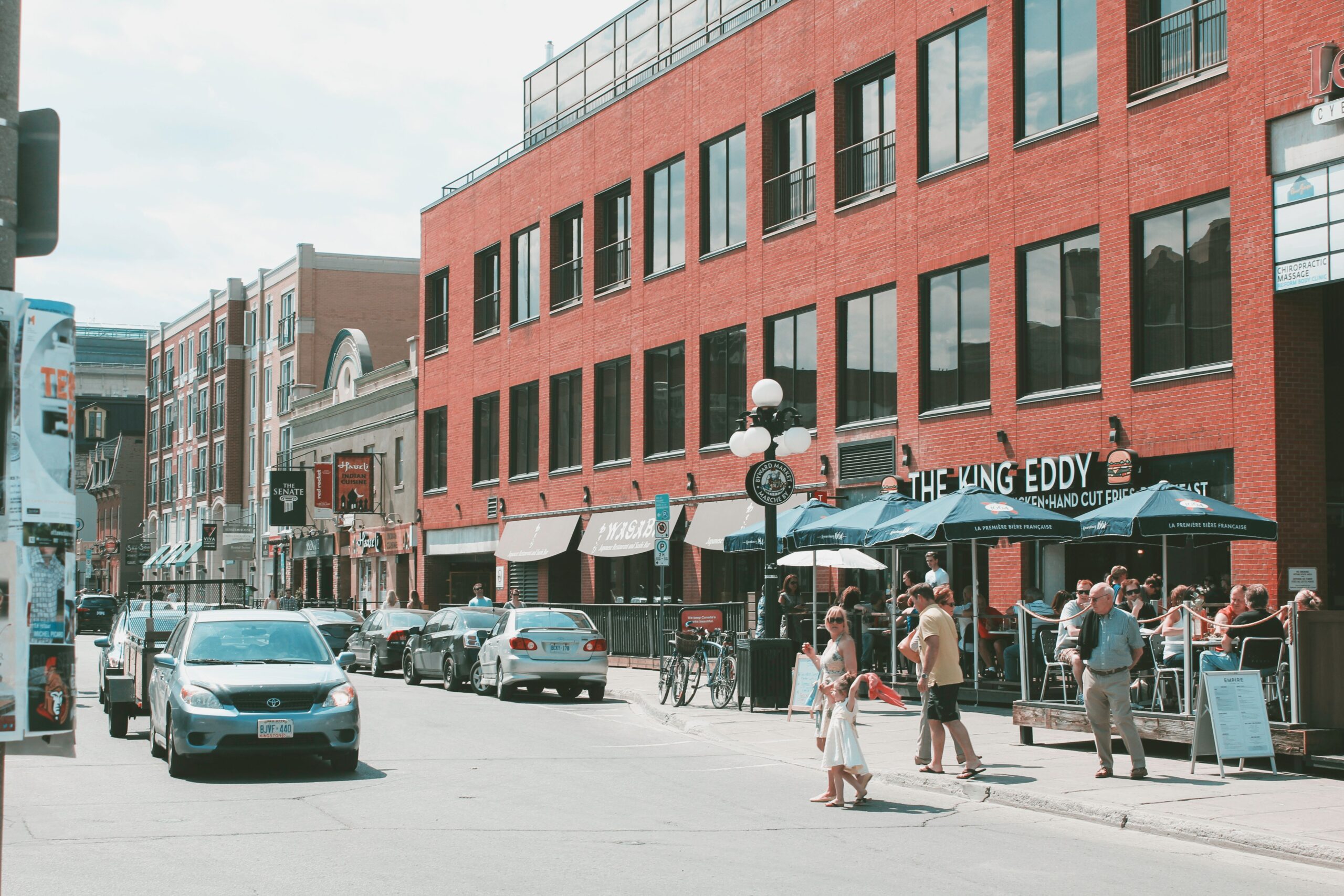 Red brick building on a street with vehicles and people passing by in Liberty Village.